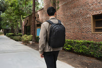 Hombre caminando al aire libre con una mochila negra cerca de un edificio de ladrillos