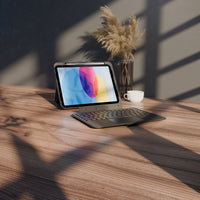 A tablet in a dark gray protective case with an attached keyboard and trackpad, set on a wooden desk with warm sunlight and shadows, next to a vase of dried grass and a small white cup.