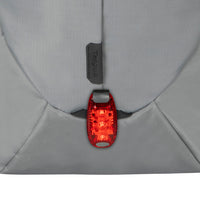 A close-up of a red bicycle tail light attached to the back of a gray backpack, with the brand name 'Targus' visible on a small black tag above it.