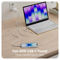 A white USB-C charging cable plugged into a wall outlet and connected to a silver laptop, with a smartphone charging on the desk. The scene is set on a light wood desk with a white rounded square border and text at the bottom reading 'Fast 45W USB-C Power Power everyday devices, faster.