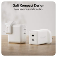 Two compact white GaN power adapters on a light wood surface with a soft neutral background. Text at the top reads 'GaN Compact Design' and 'More power in a smaller design.